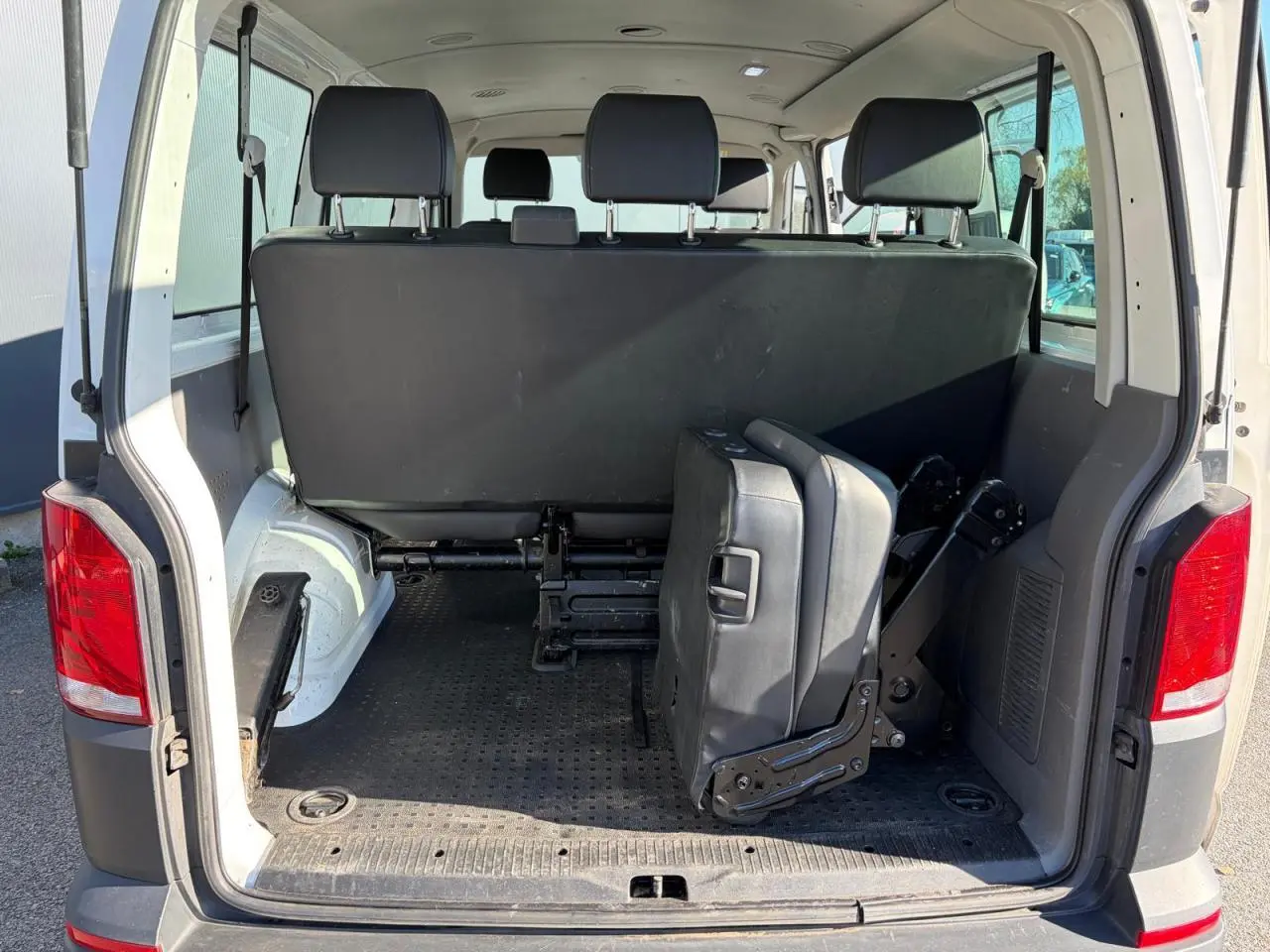 Vue arrière ouverte du Volkswagen Transporter T6 Minibus blanc, montrant les sièges rabattus et l'espace de chargement intérieur.