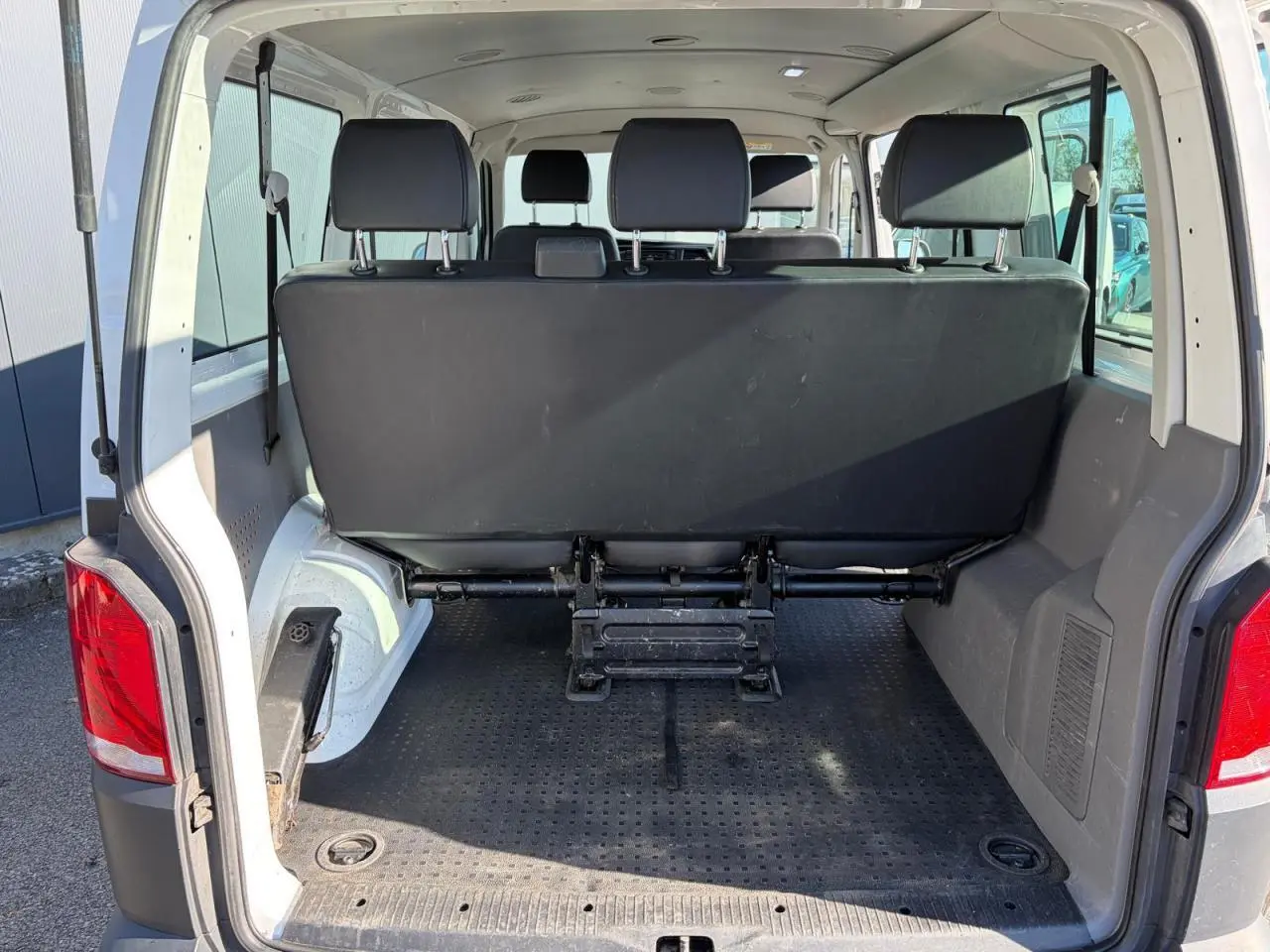 Vue arrière du Volkswagen Transporter T6 blanc, coffre ouvert montrant la banquette arrière et l'espace de chargement.