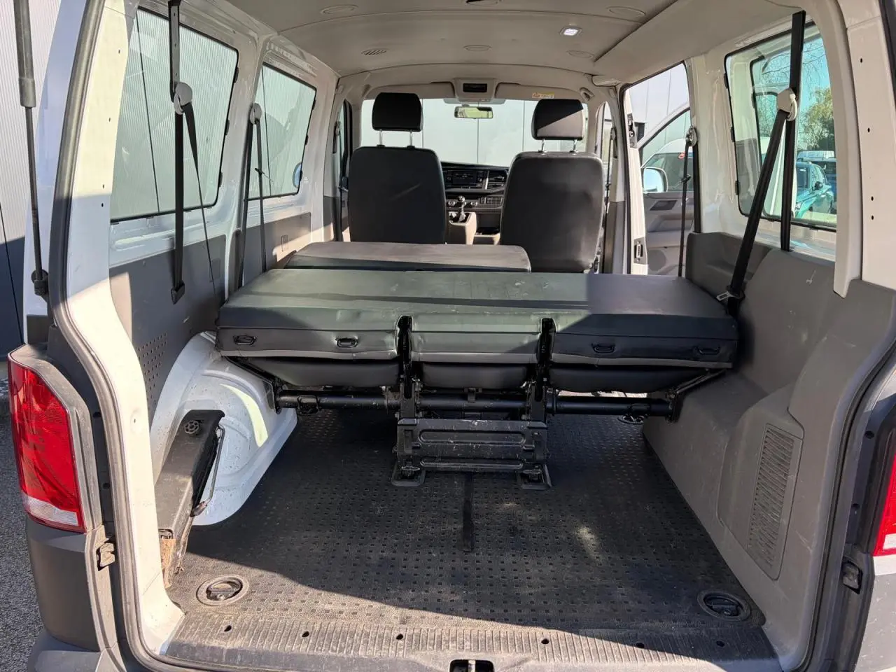 Intérieur arrière du Volkswagen Transporter T6 blanc, vue de la porte ouverte avec banquette rabattue et espace de chargement visible.