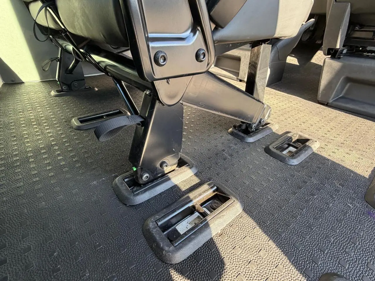Gros plan sur le système d'ancrage des sièges noirs dans l'habitacle du Volkswagen Transporter T6 blanc.
