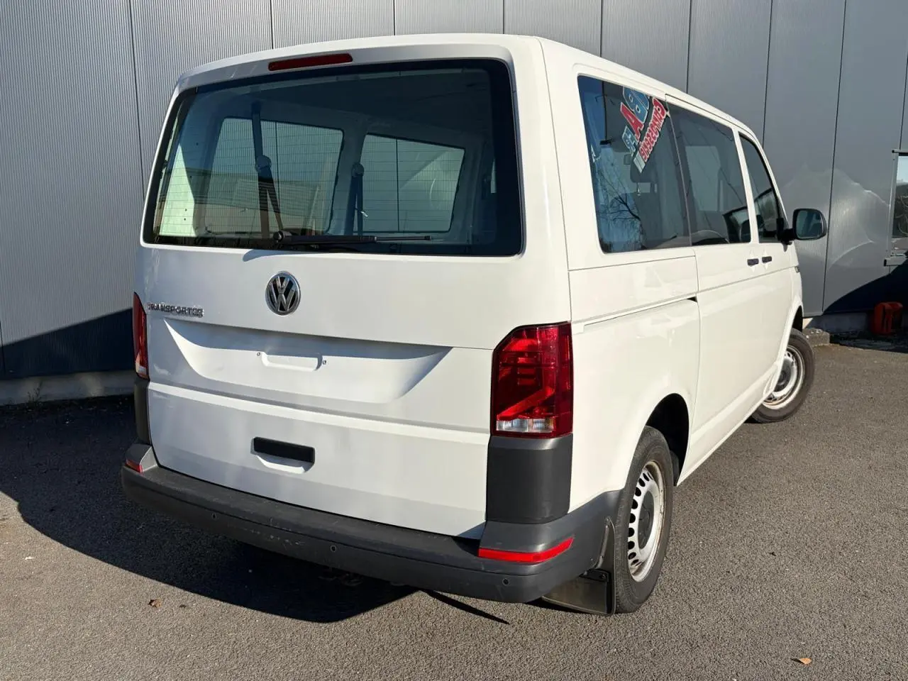 Vue 3/4 arrière droite d'un Volkswagen Transporter T6 Minibus blanc avec vitres teintées et feux arrière rouges.