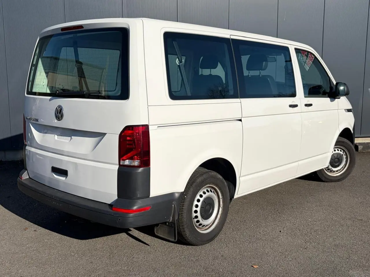 Vue 3/4 arrière droite d’un Volkswagen Transporter T6 Minibus blanc, avec porte coulissante et jantes acier.