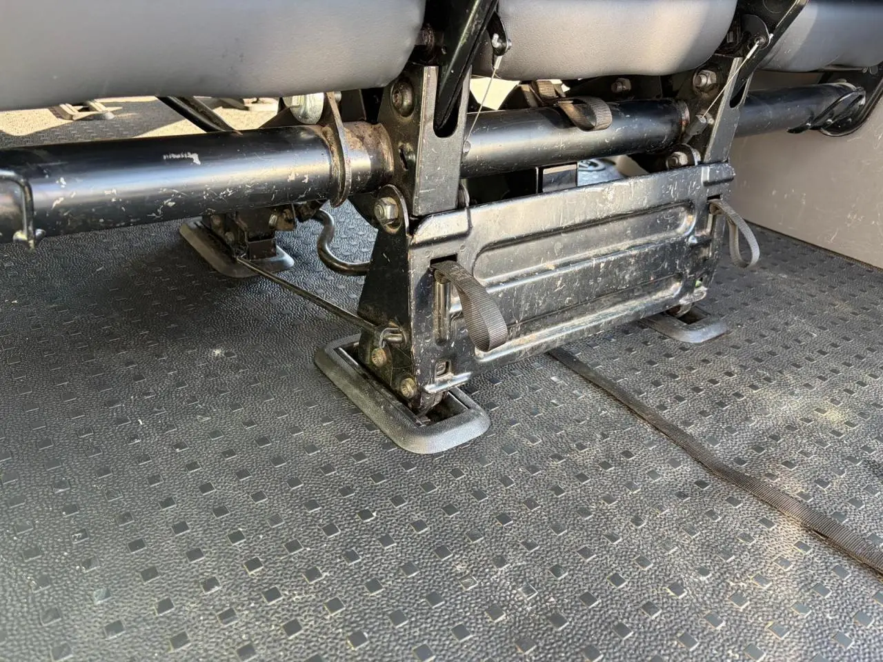 Gros plan sous les sièges arrière du Volkswagen Transporter T6 Minibus blanc, montrant la fixation et la structure métallique.