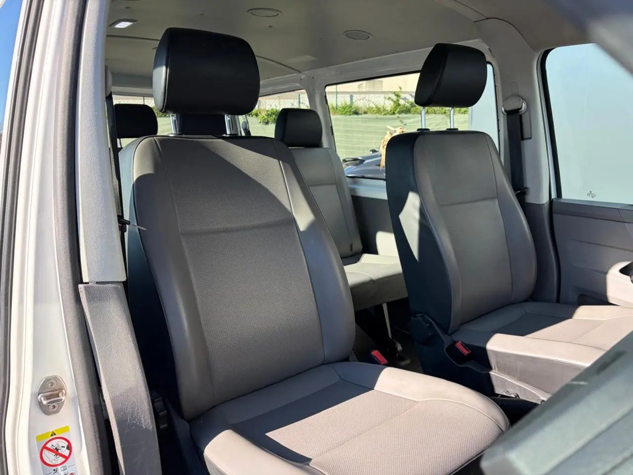 Vue intérieure côté droit du Volkswagen Transporter T6 Minibus blanc, montrant les sièges avant et arrière en tissu gris.