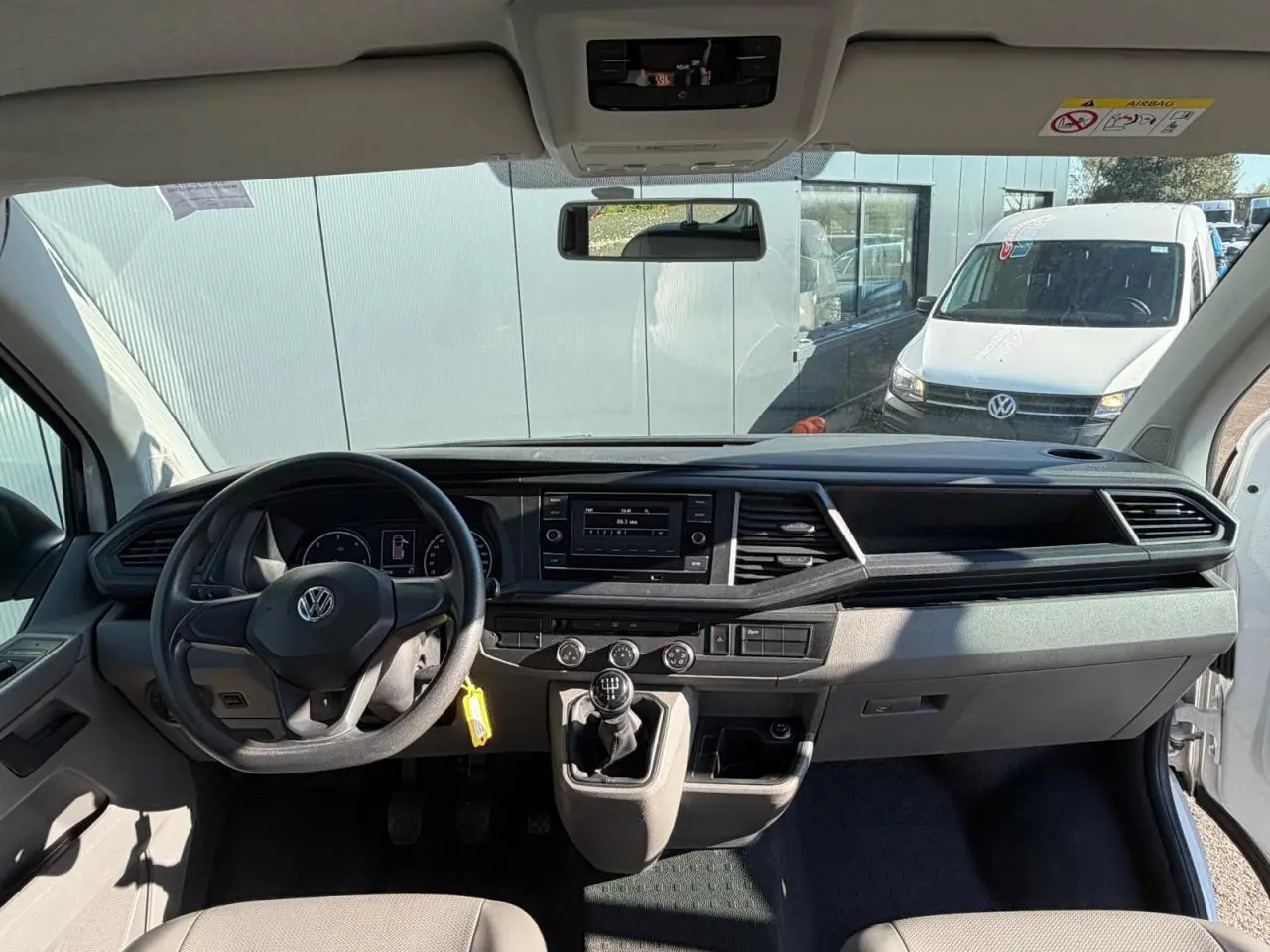 Vue intérieure avant du Volkswagen Transporter T6 Minibus blanc, montrant le tableau de bord et la boîte manuelle.