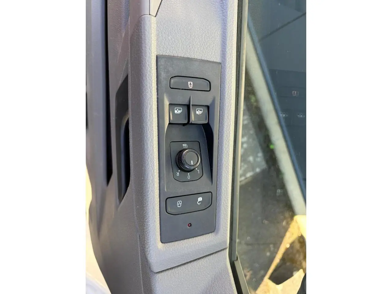 Gros plan sur les commandes des rétroviseurs et des vitres côté conducteur du Volkswagen Transporter T6 blanc.