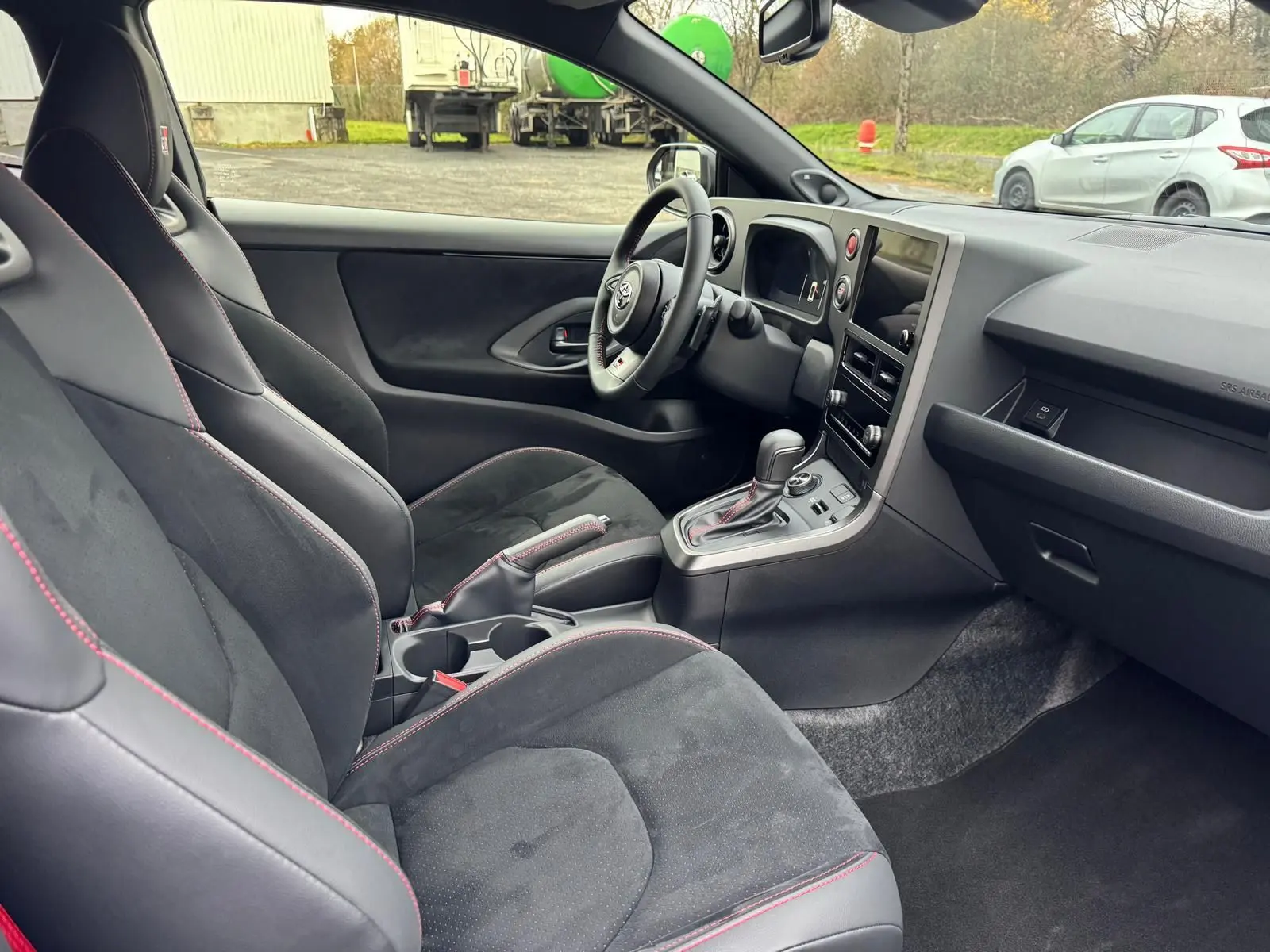 Vue intérieure côté conducteur de la Toyota Yaris GR avec sièges sport noirs et surpiqûres rouges visibles.