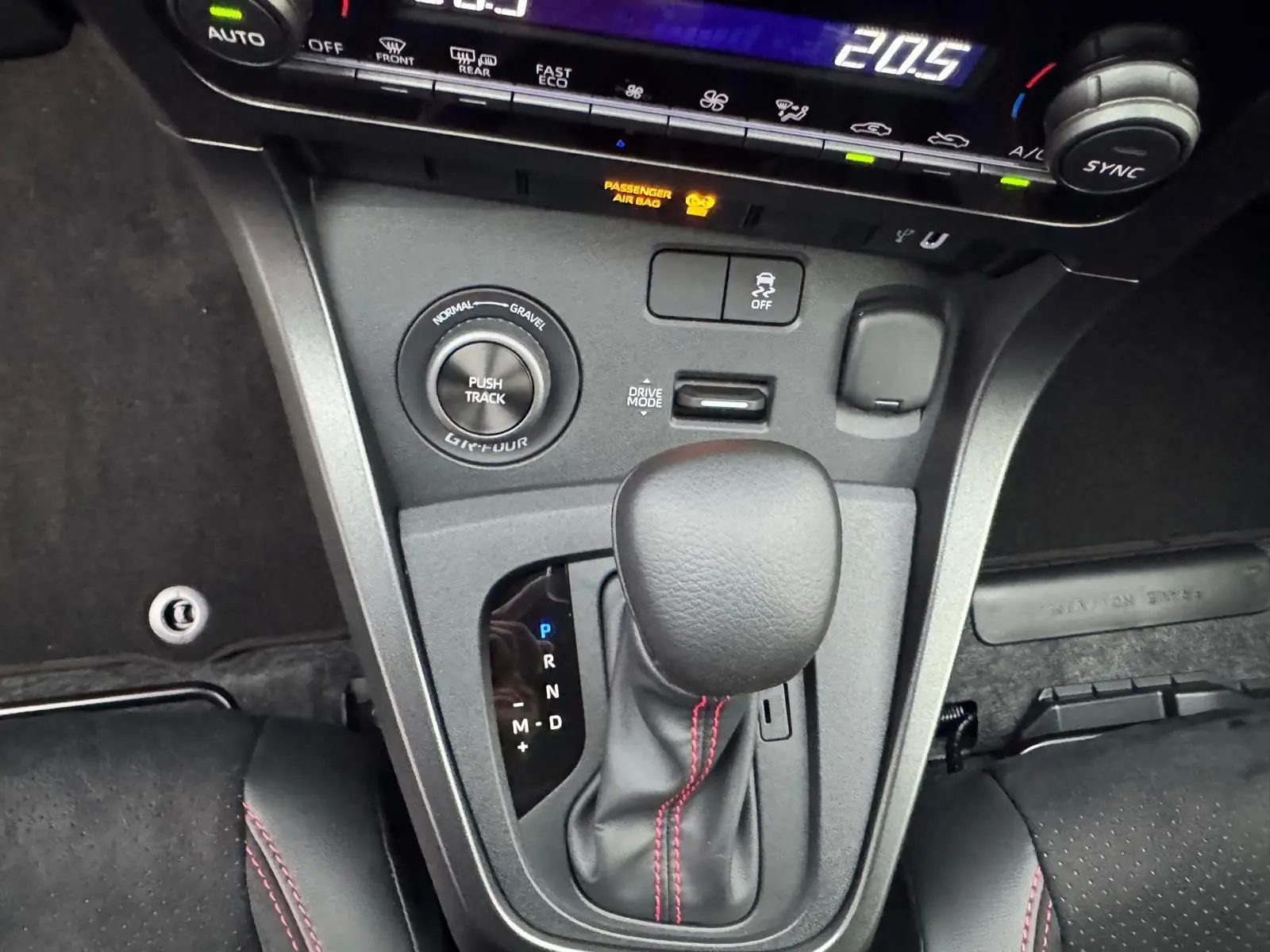 Gros plan sur la console centrale de la Toyota Yaris GR avec levier de vitesses et surpiqûres rouges visibles.