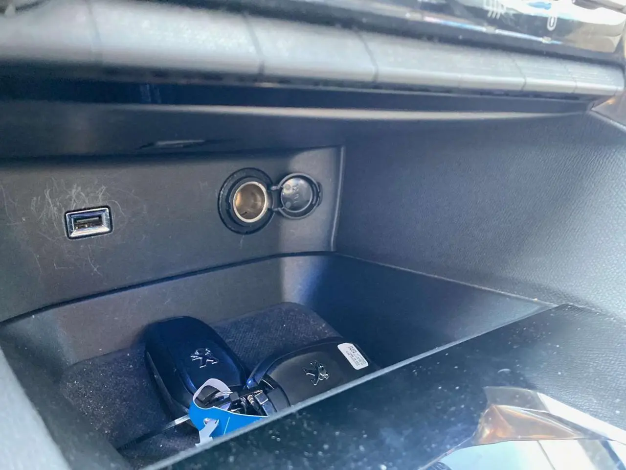 Gros plan sur la boîte à gants ouverte du Peugeot 3008 blanc, montrant deux clés et une prise USB.
