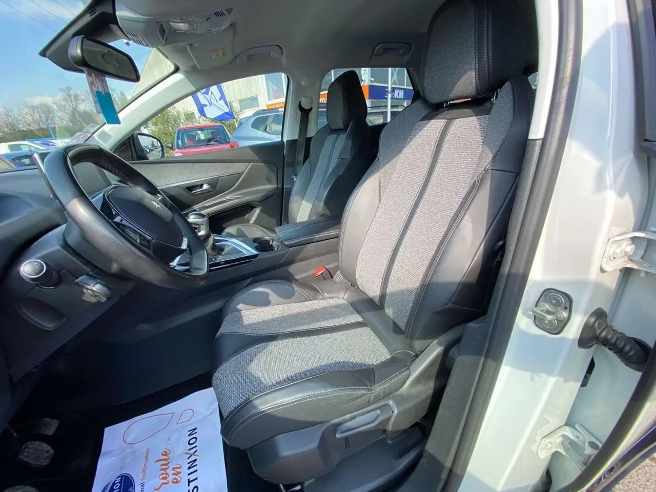 Vue intérieure côté conducteur du Peugeot 3008 blanc, montrant les sièges bi-matière et le volant multifonction.
