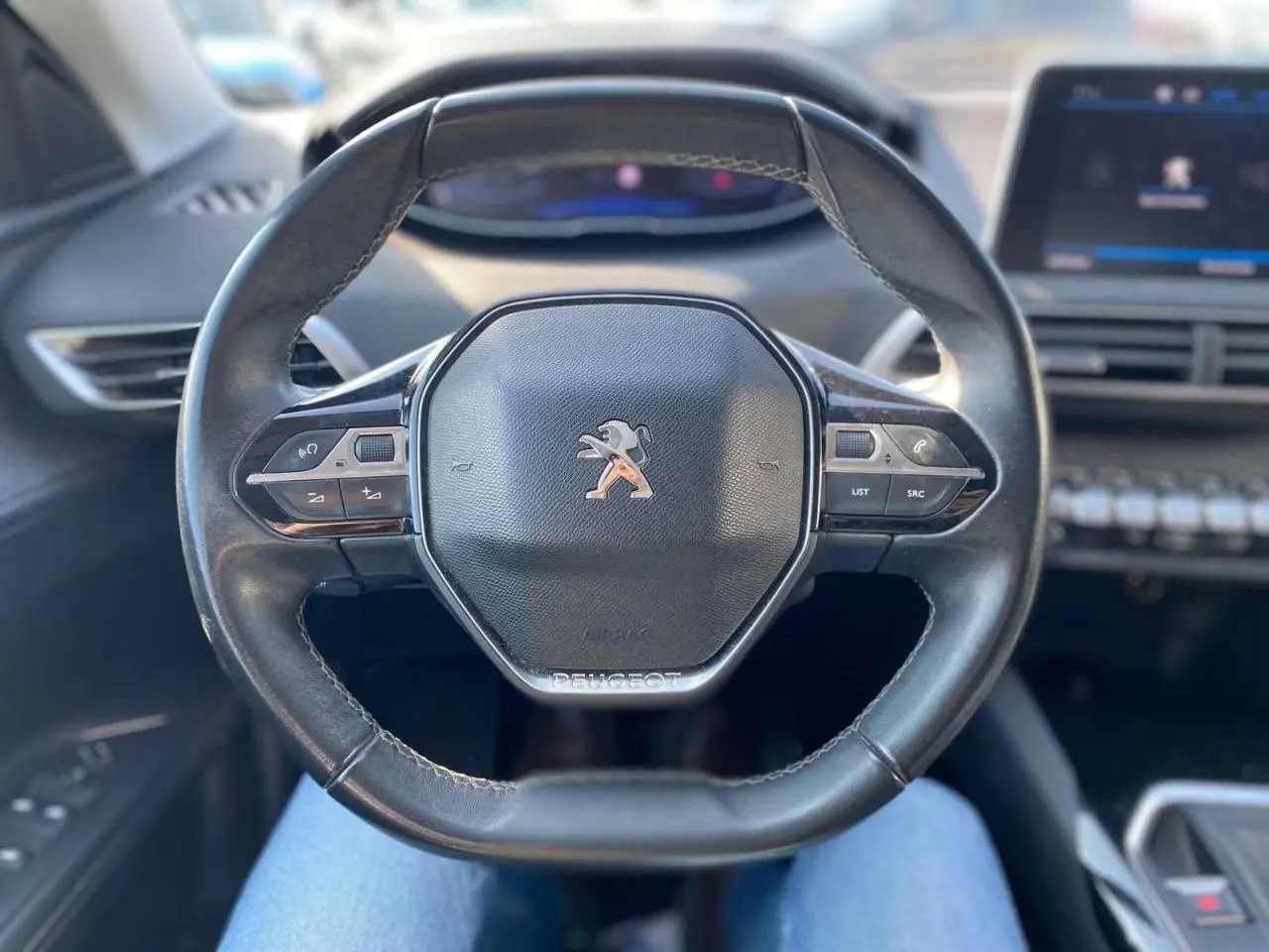 Vue rapprochée du volant cuir noir du Peugeot 3008 2018 avec commandes intégrées et tableau de bord flou en arrière-plan.