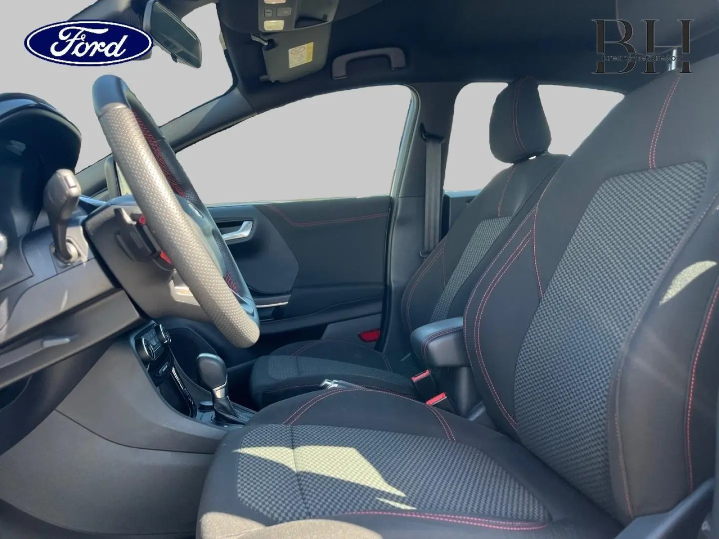 Vue intérieure côté conducteur du Ford Puma 2022, sièges noirs avec surpiqûres rouges et volant sport multifonction.