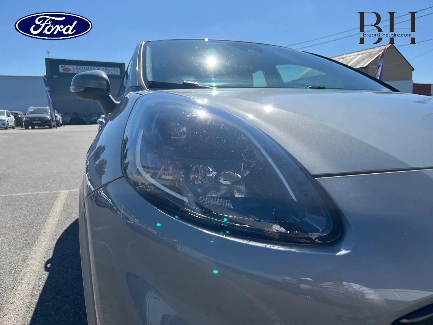 Gros plan sur le phare avant gauche du Ford Puma gris Solar métallisé sous un ciel ensoleillé.