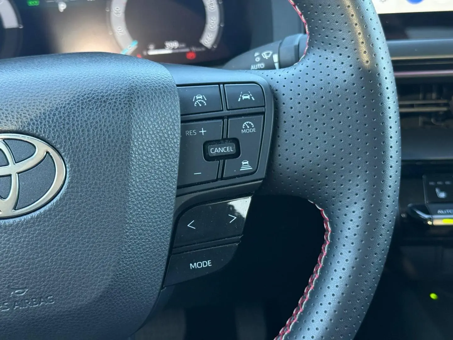 Gros plan sur le volant perforé noir avec surpiqûres rouges du Toyota C-HR 2.0 Hybride GR Sport 2025, boutons multifonctions visibles.