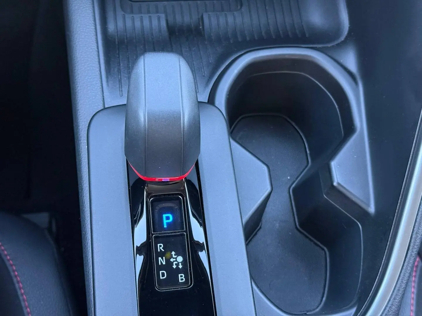 Gros plan sur la console centrale du Toyota C-HR 2.0 Hybride 200ch GR Sport, levier de vitesse et porte-gobelets noirs.