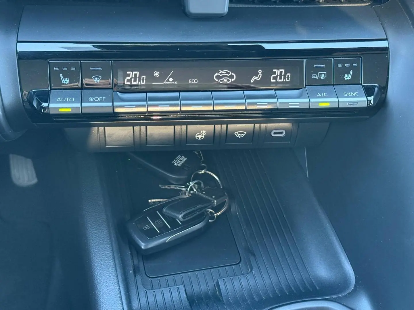 Vue rapprochée de la console centrale du Toyota C-HR 2025, montrant les commandes de climatisation et un porte-clés noir posé.
