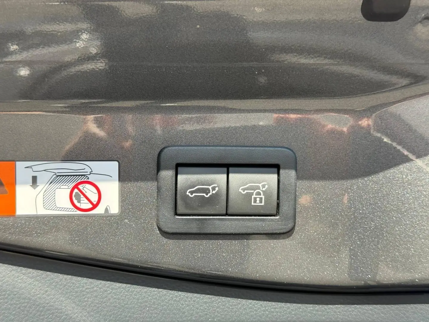 Gros plan sur les boutons d'ouverture et de verrouillage du coffre sur la garniture gris atlas métallisé du Toyota C-HR 2025.