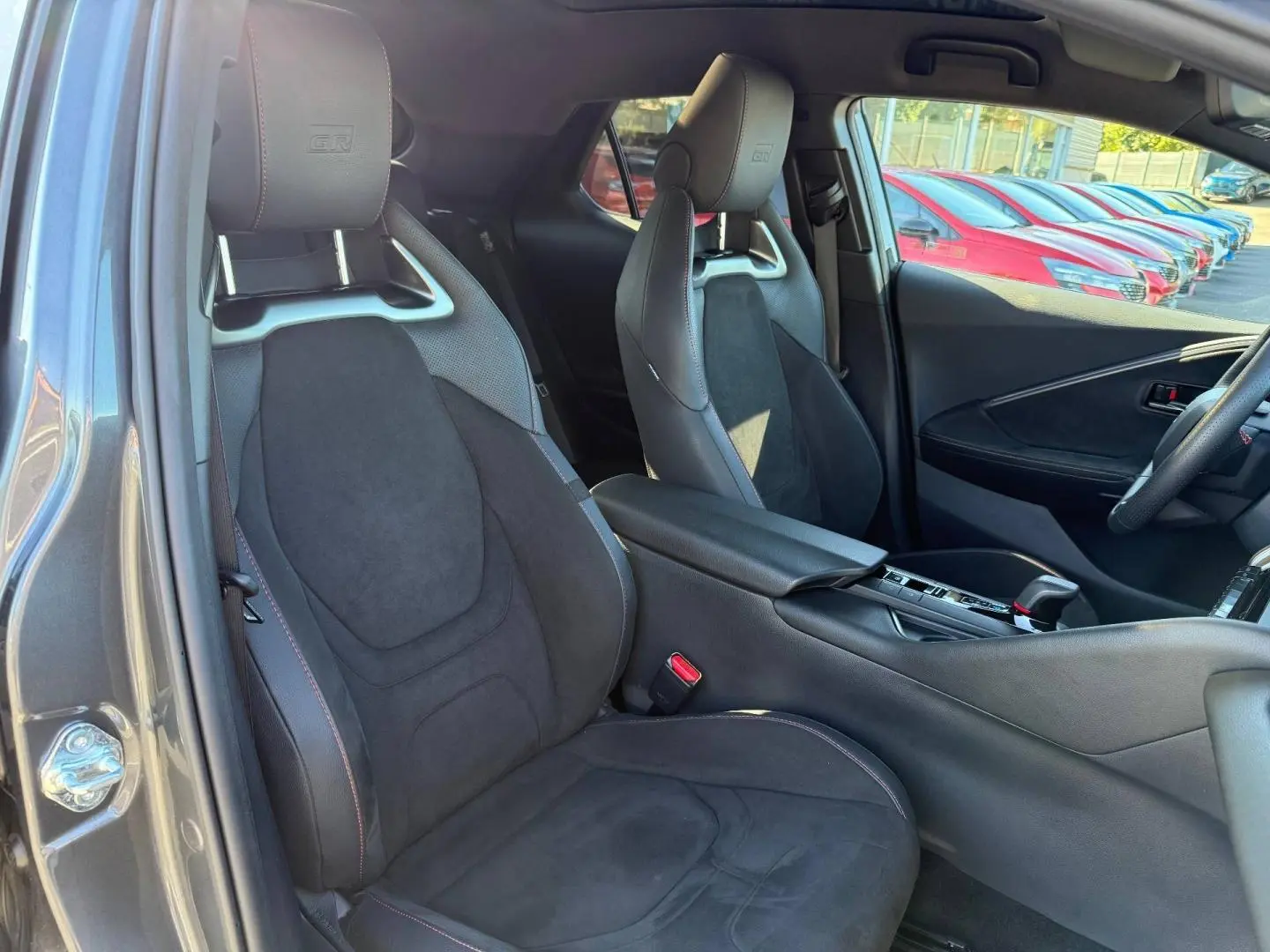 Intérieur avant du Toyota C-HR GR Sport 2025, sièges sport noirs avec logo GR et surpiqûres rouges visibles.