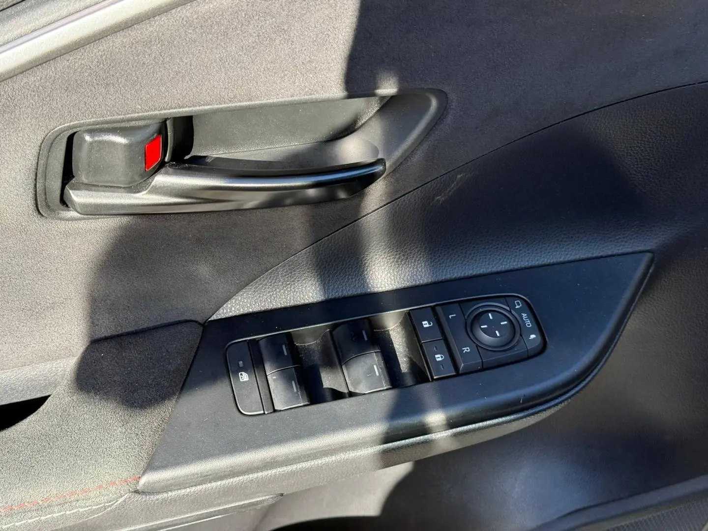Gros plan sur la commande des vitres et la poignée intérieure noire du côté gauche d’une Toyota C-HR gris Atlas bi-ton.