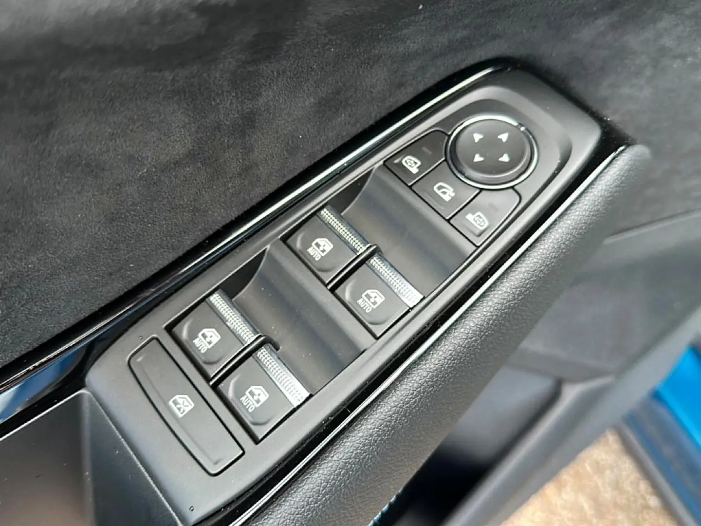 Gros plan sur les commandes des vitres électriques côté gauche d'une Renault Austral bleu outremer, avec boutons noirs et finition cuir.