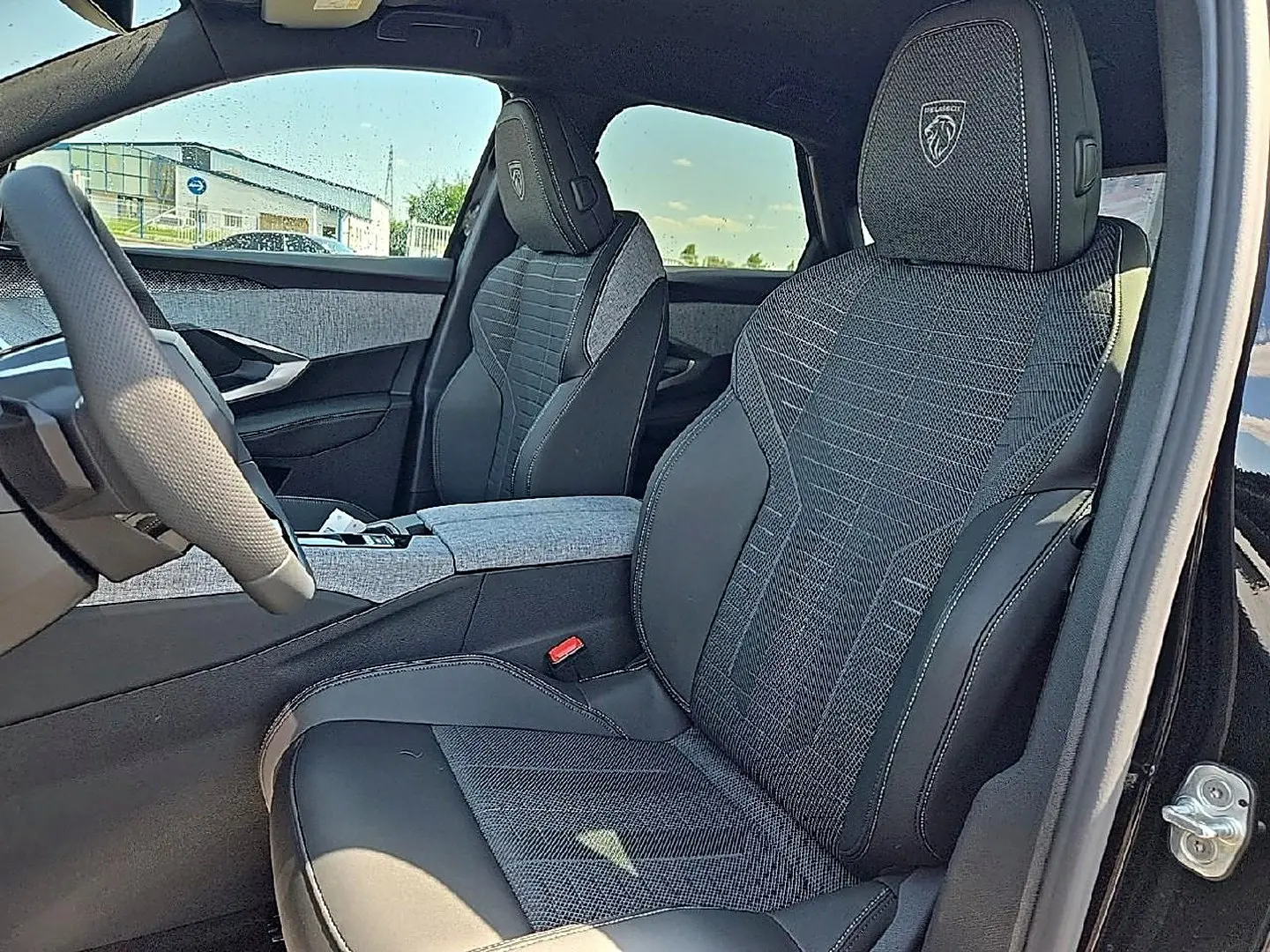 Vue intérieure côté conducteur du Peugeot 3008 noir 2026, sièges tissu et cuir avec logo Peugeot brodé sur appuie-tête.
