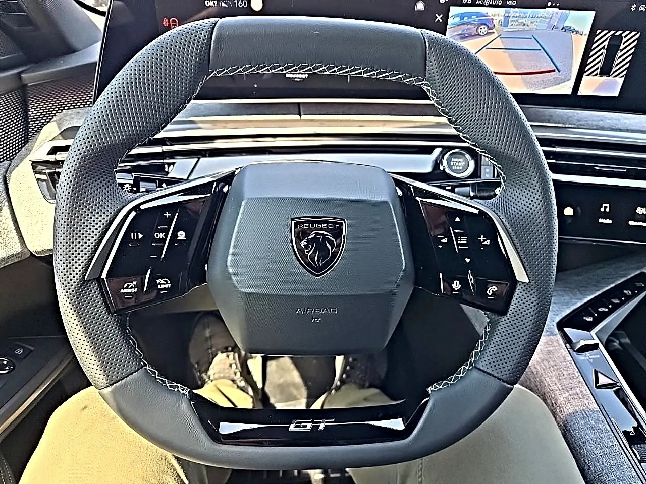 Vue intérieure centrée sur le volant cuir noir perforé du Peugeot 3008 1.2 hybrid GT avec commandes multifonctions et logo GT.