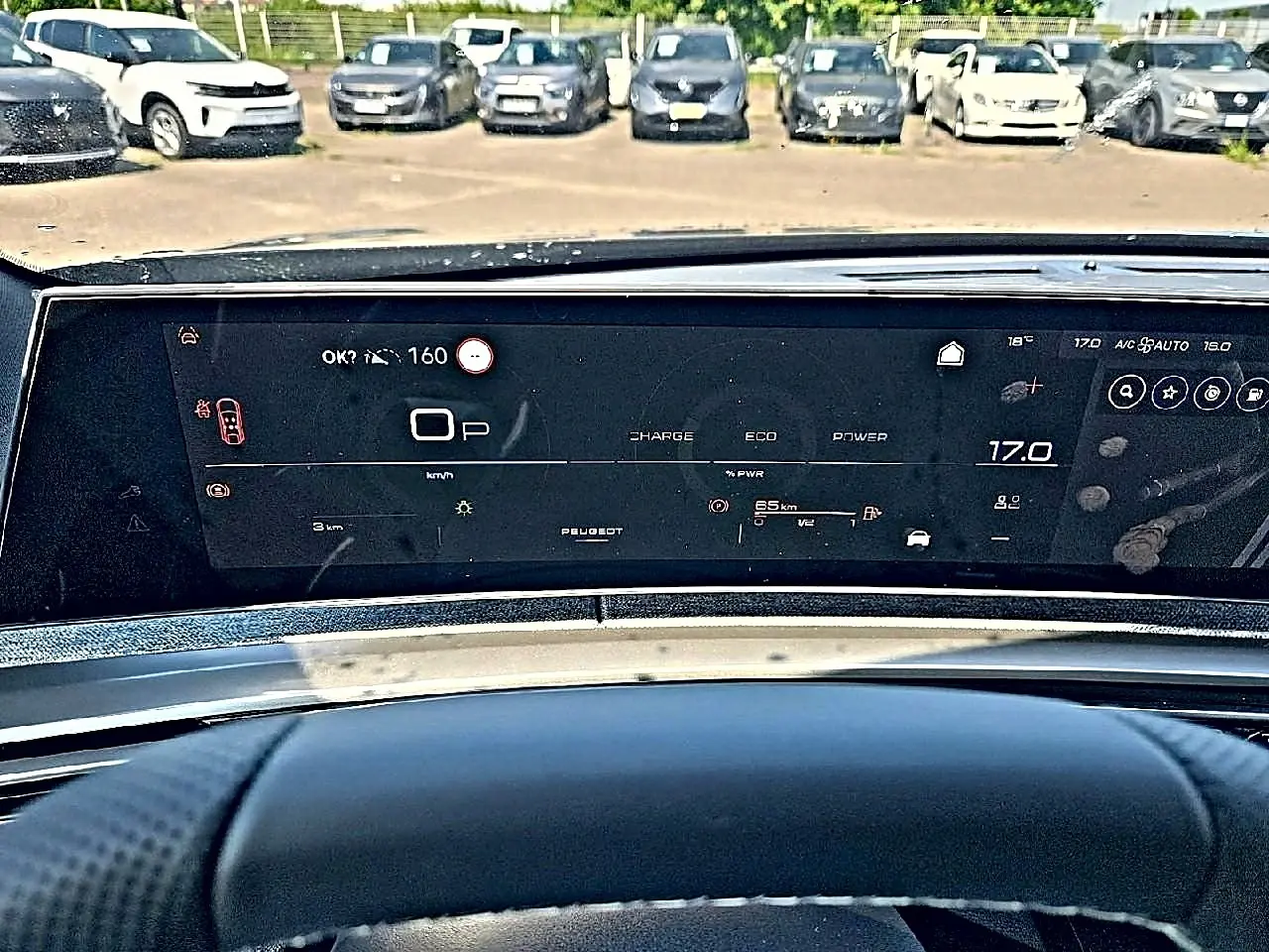 Vue intérieure du tableau de bord numérique du Peugeot 3008 noir, affichant la vitesse et la température, avec parking en arrière-plan.