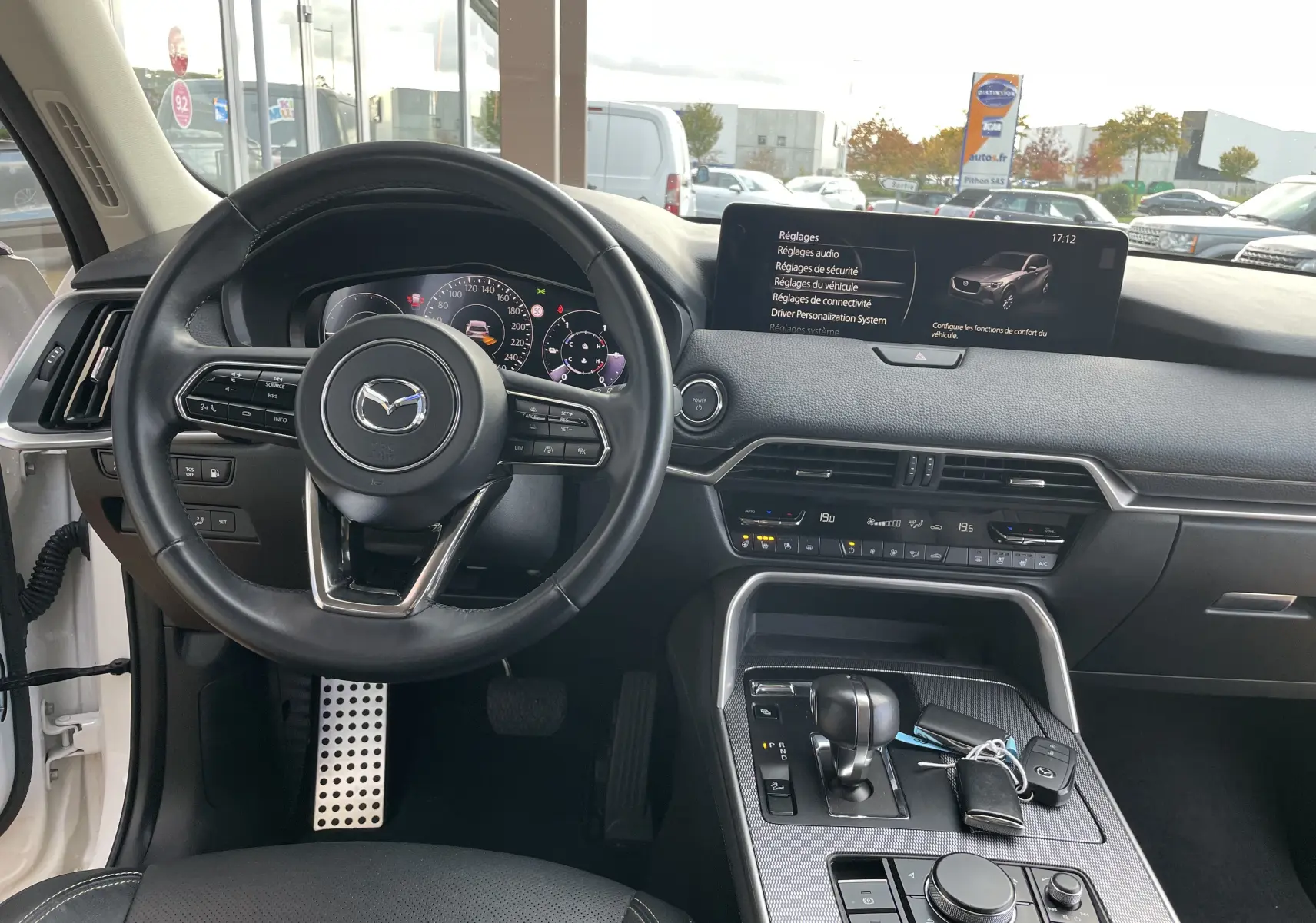 Vue intérieure du tableau de bord et volant noir du Mazda CX-60 blanc nacré, avec écran tactile et console centrale moderne.