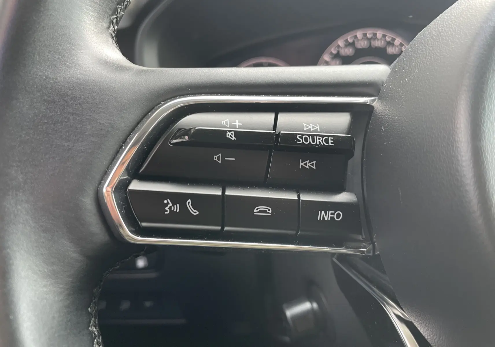 Gros plan sur les commandes multifonctions noires du volant côté gauche du Mazda CX-60 blanc nacré 2023.