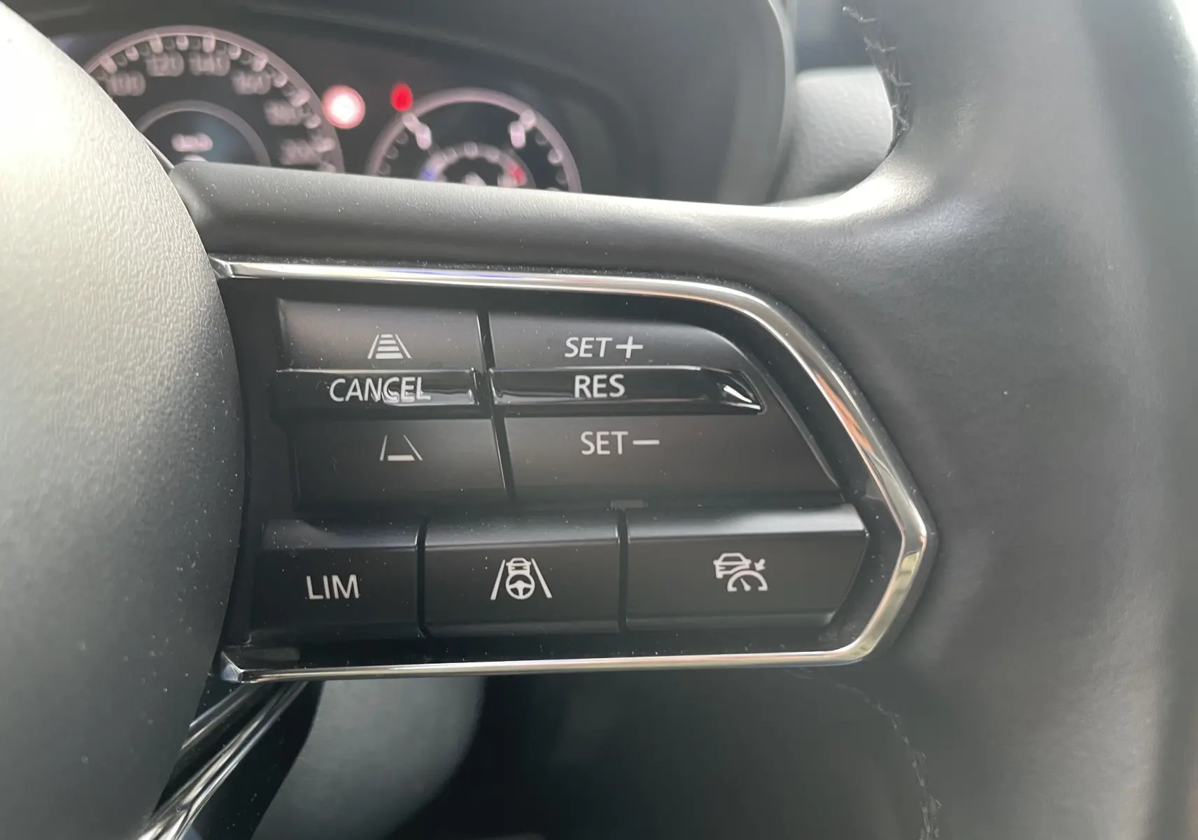 Gros plan sur les commandes de régulateur de vitesse au volant du Mazda CX-60 2023 blanc nacré, intérieur gris noir.