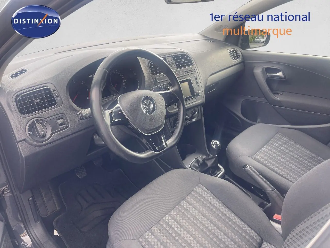 Vue intérieure côté conducteur de la Volkswagen Polo noire 2016, montrant le volant, la boîte manuelle et les sièges tissu gris.