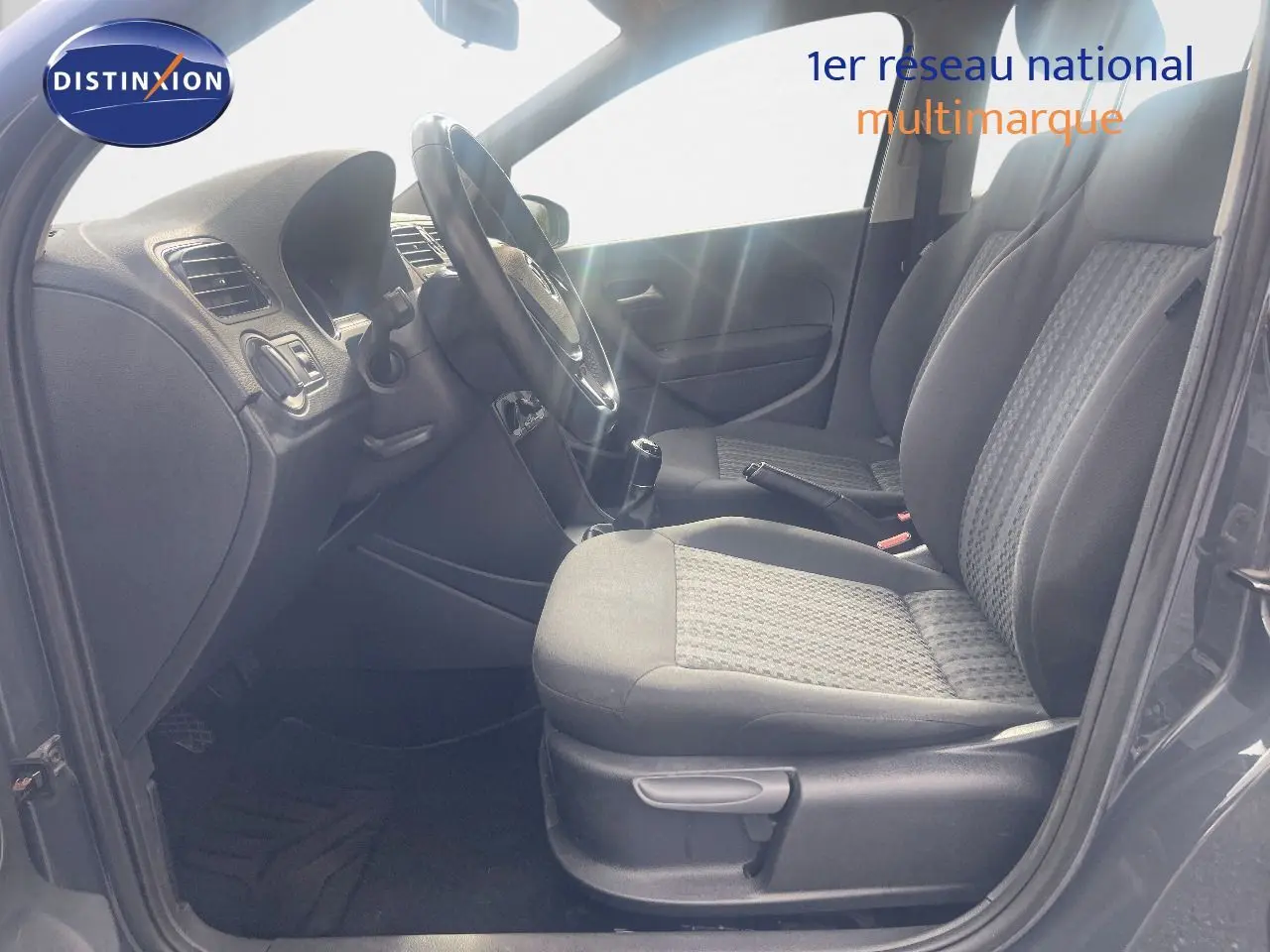 Vue intérieure côté conducteur de la Volkswagen Polo noire 2016, montrant les sièges avant et le volant avec boîte manuelle.