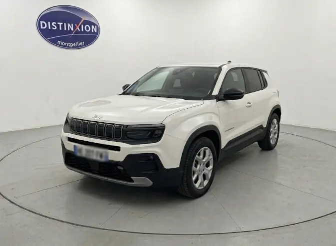 Jeep Avenger blanc en 3/4 avant droit, avec calandre noire distinctive et jantes argentées, sur fond neutre intérieur.