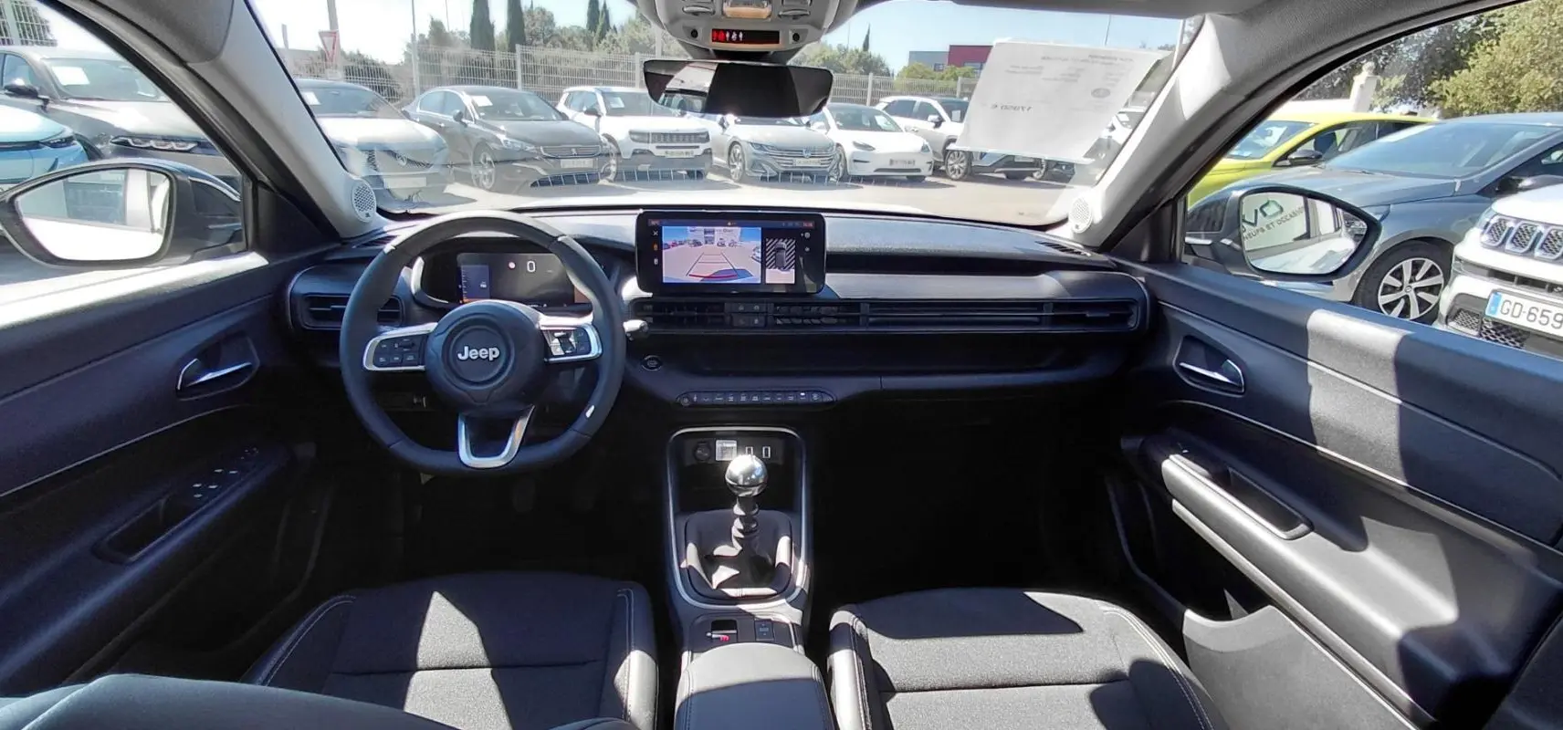 Vue intérieure avant du Jeep Avenger 2025, tableau de bord noir avec écran tactile et levier de vitesse manuel visible.