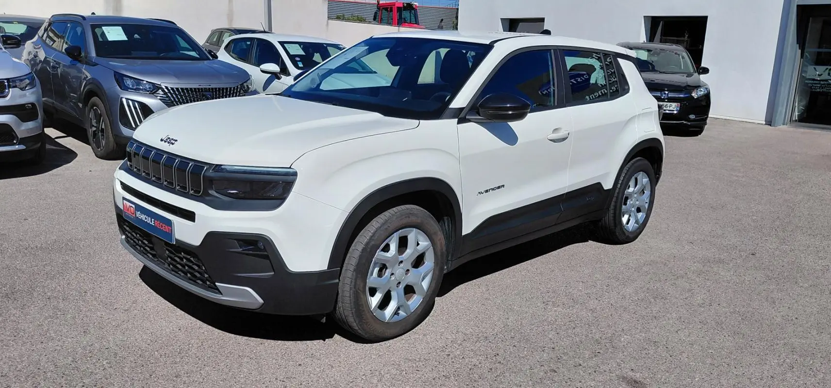 Jeep Avenger blanc en vue 3/4 avant droit, avec calandre noire distinctive et jantes argentées, stationné en extérieur.