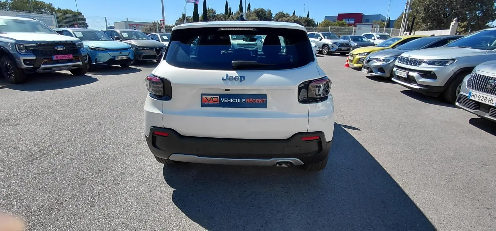 Vue arrière d'un Jeep Avenger blanc 2025 avec feux arrière sombres et plaque "Véhicule récent" sur parking.