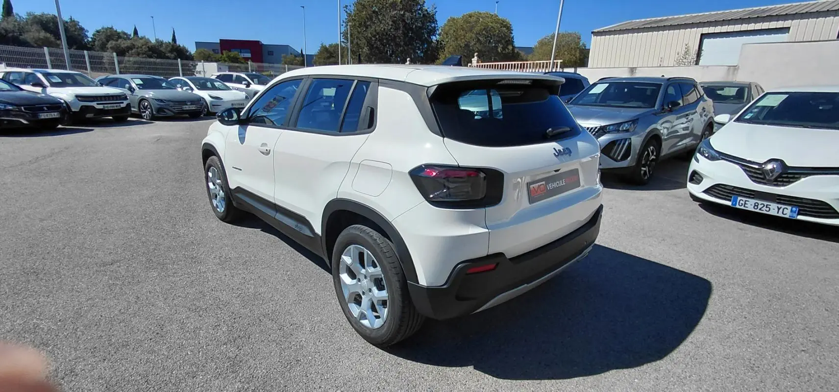 Jeep Avenger blanc en 3/4 arrière droit, avec feux arrière noirs et jantes argentées, stationné en extérieur.