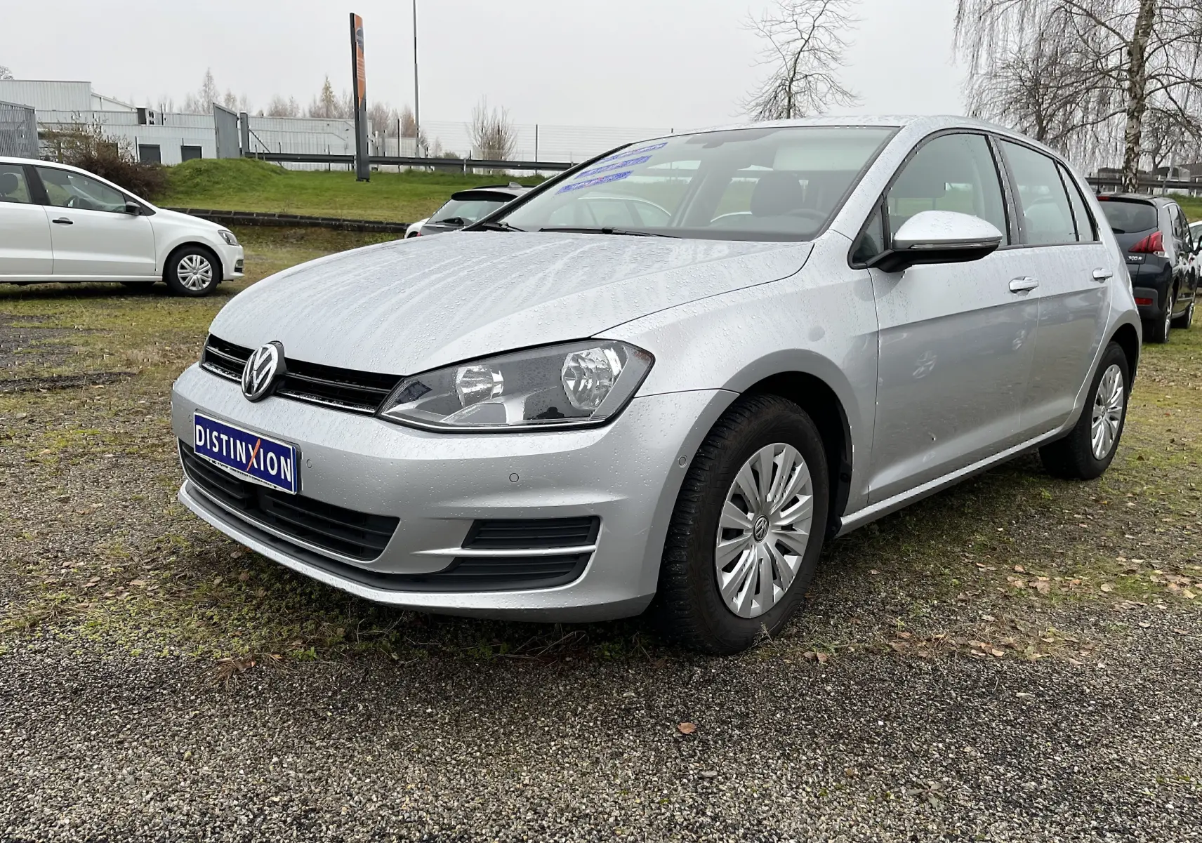 Volkswagen Golf 7 argent vue 3/4 avant droit sur parking avec plaque Distinxion visible.