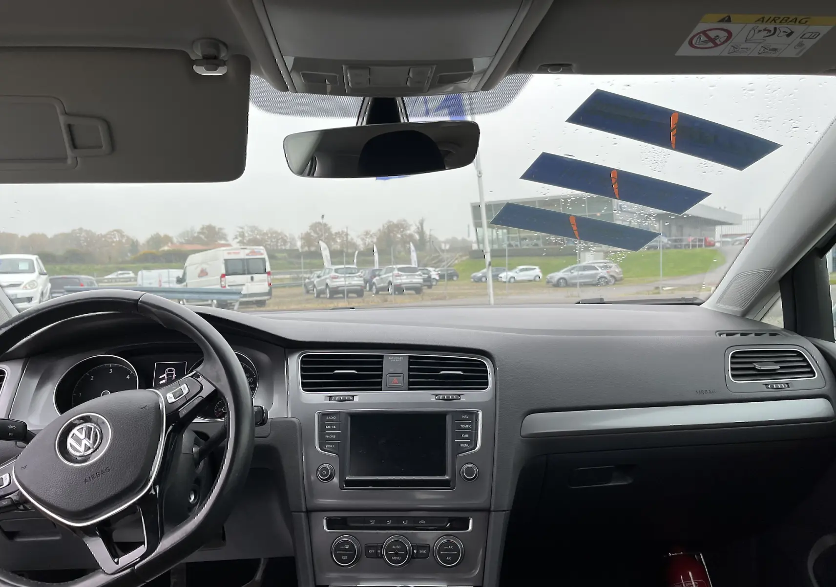 Vue intérieure avant du tableau de bord noir et volant Volkswagen d'une Golf 7 argent, avec écran tactile et commandes visibles.