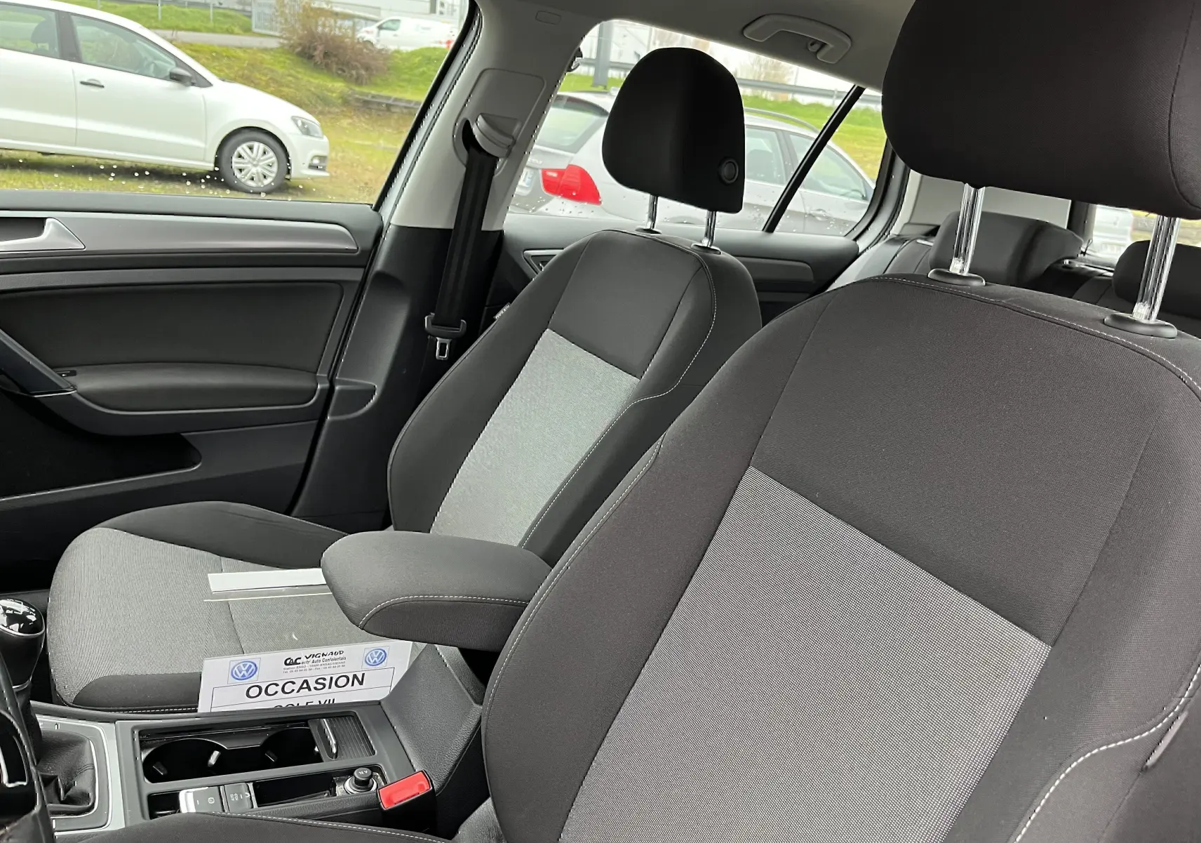 Vue intérieure de la Golf 7 2017 montrant les sièges avant en tissu noir et gris avec accoudoir central.