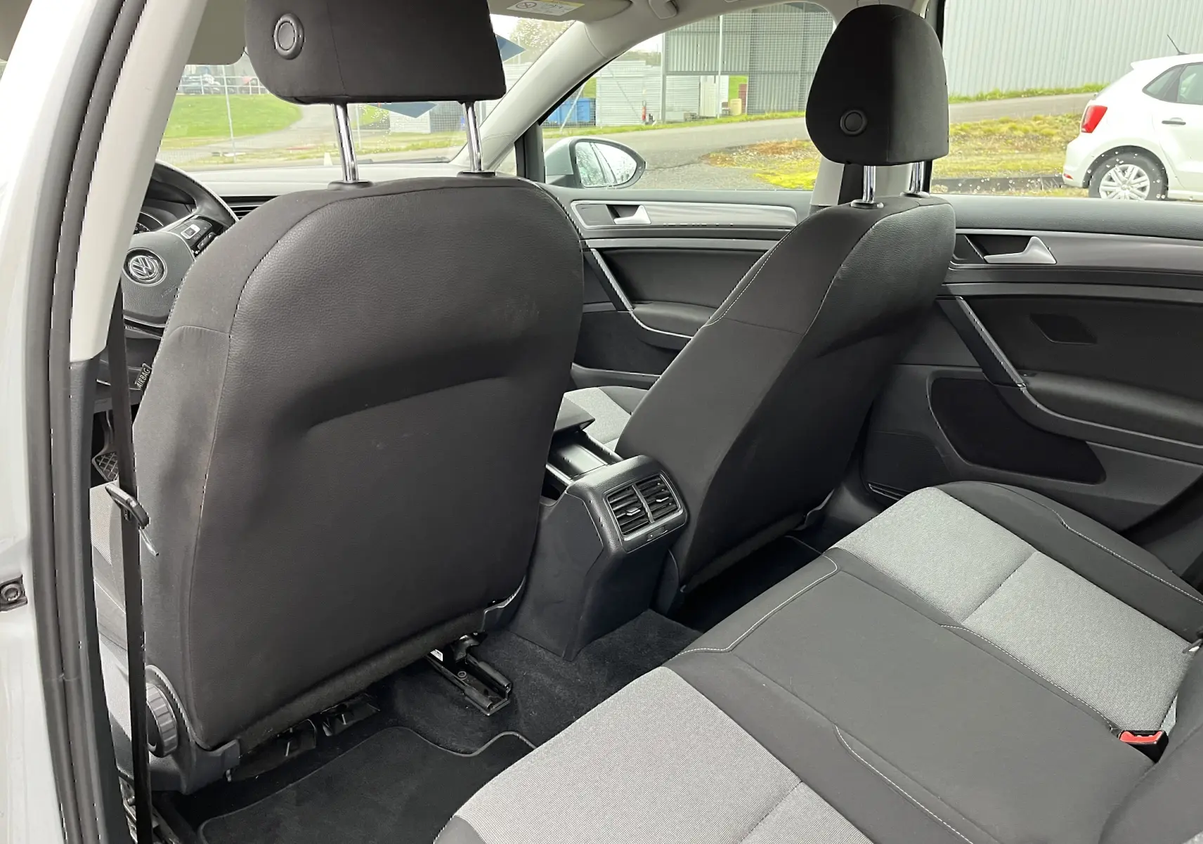 Vue intérieure arrière de la Volkswagen Golf 7 argent, sièges tissu noir et gris avec aérateurs centraux visibles.