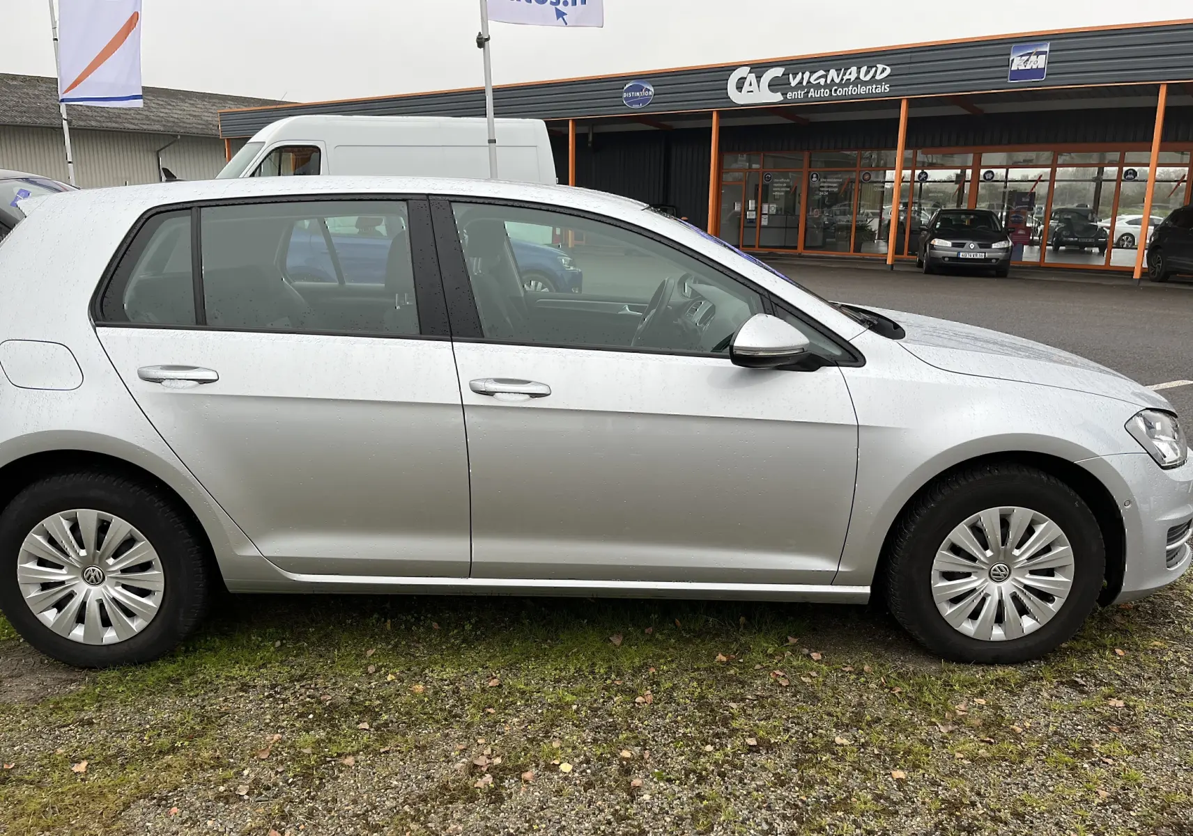 Vue latérale droite d'une Volkswagen Golf 7 argentée de 2017 garée devant un bâtiment commercial.