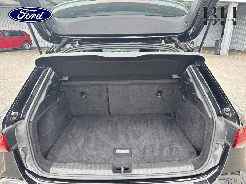 Coffre ouvert vu de l'arrière d'une Audi A3 Sportback 35 TDI noir Mythic métallisé, intérieur spacieux et tapis gris.