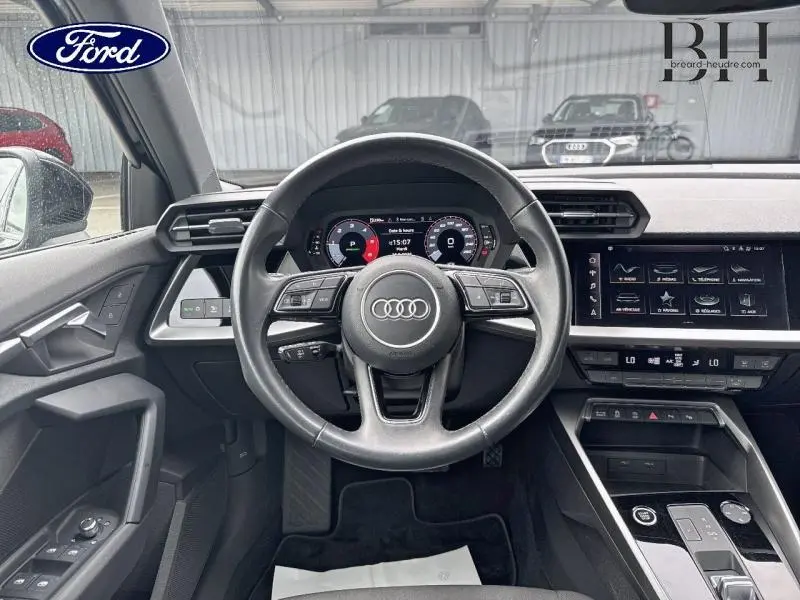Vue intérieure centrée sur le volant cuir multifonction d'une Audi A3 Sportback 35 TDI noire avec tableau de bord digital et écran tactile.