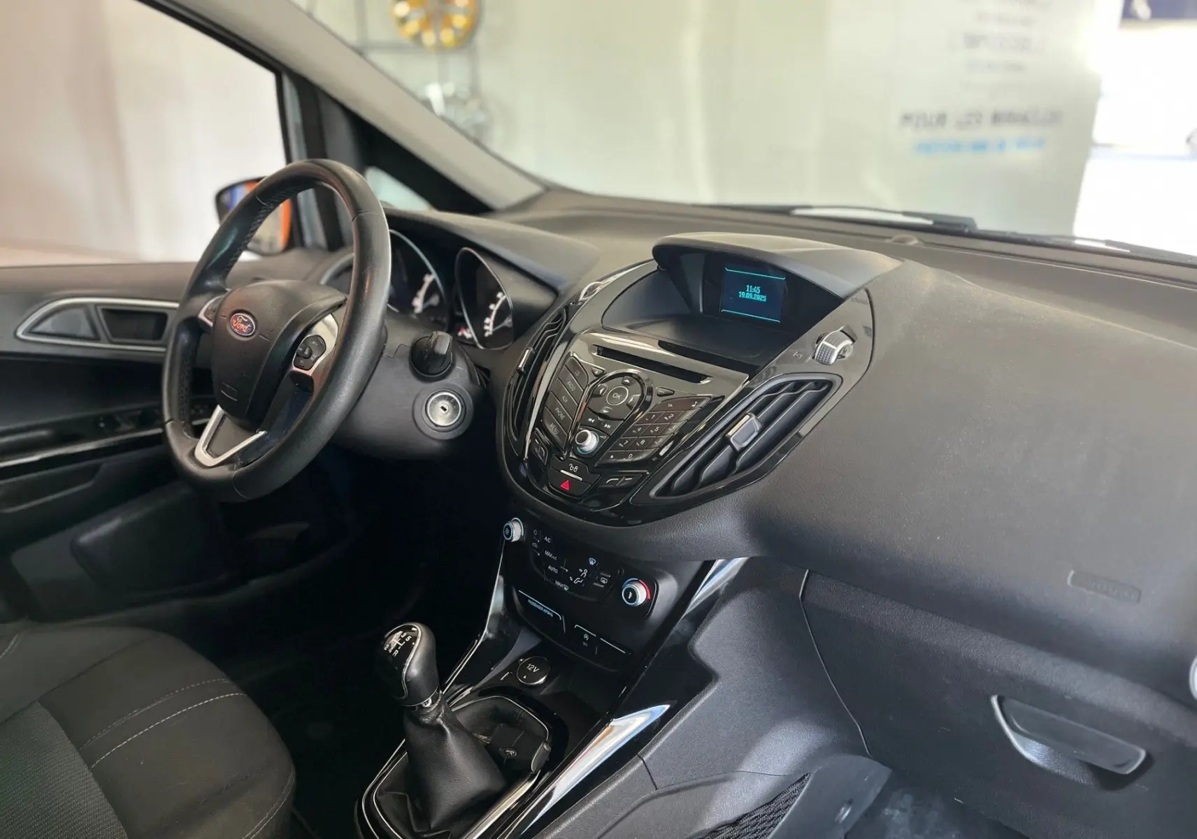 Vue intérieure côté conducteur du tableau de bord noir et levier de vitesse manuel d'une Ford B-MAX gris clair 2015.
