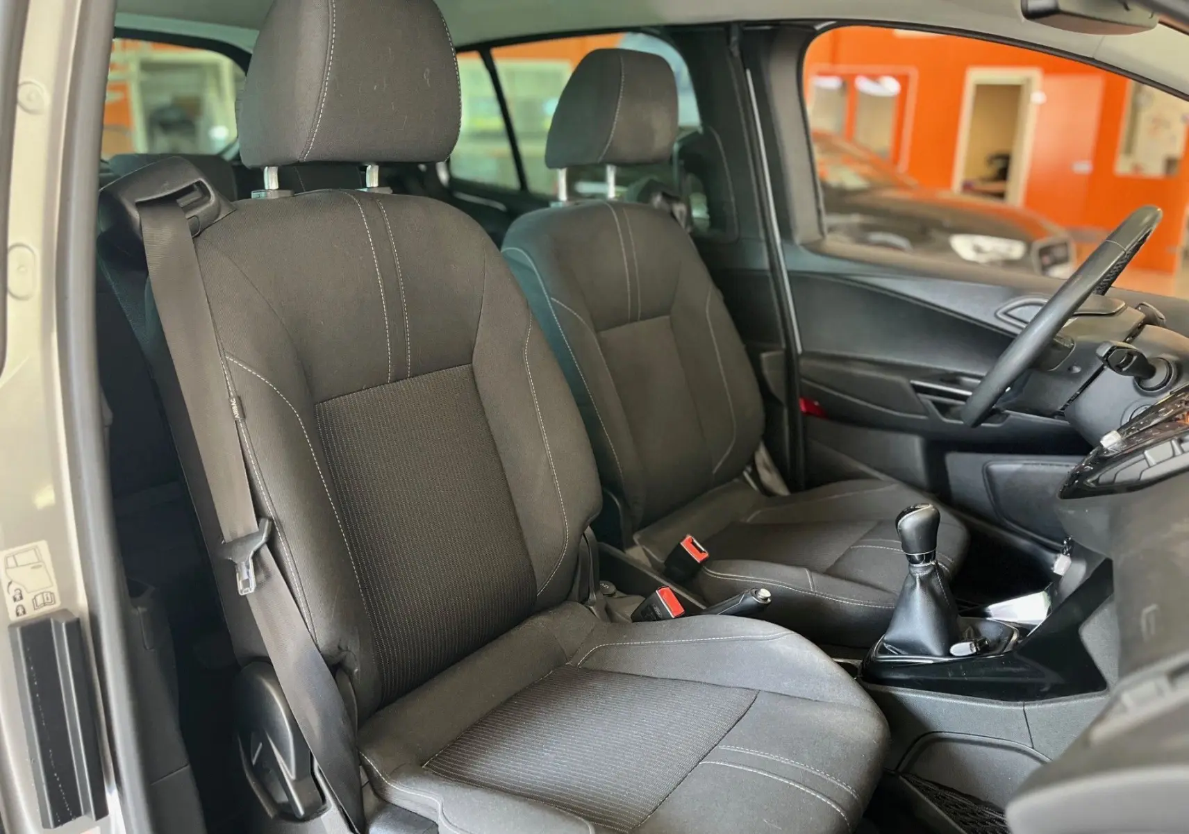 Vue intérieure de face des sièges avant noirs en tissu du Ford B-MAX gris clair avec levier de vitesse manuel visible.