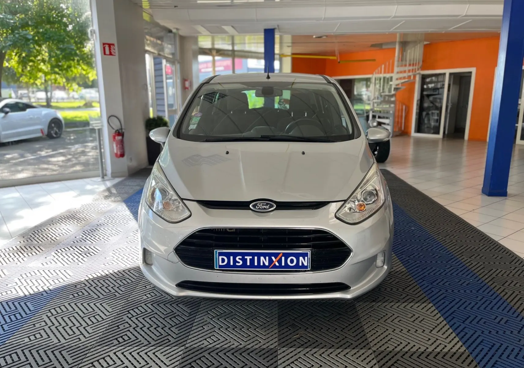Vue avant d'une Ford B-MAX gris clair 2015 dans un showroom avec une plaque Distinxion visible.