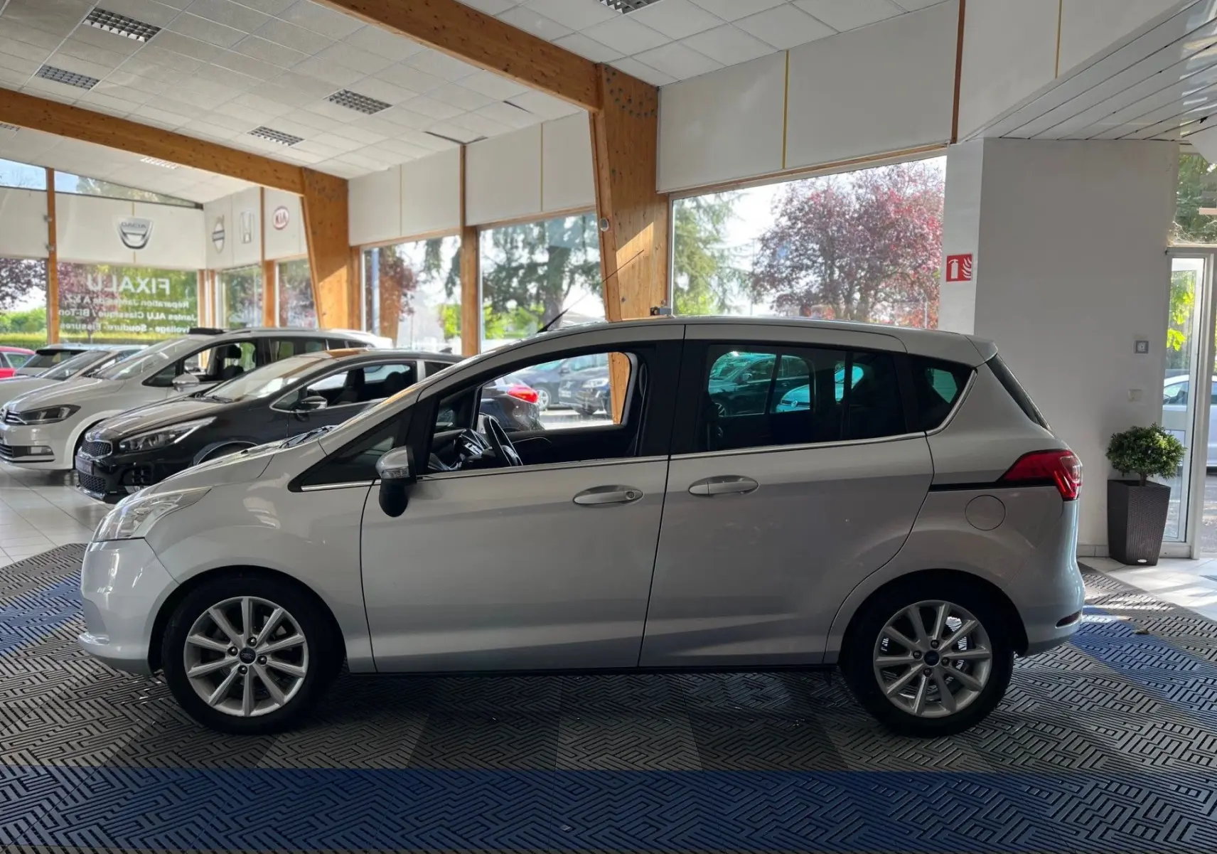 Ford B-MAX gris clair vue de profil côté gauche dans un showroom lumineux avec jantes alliage visibles.