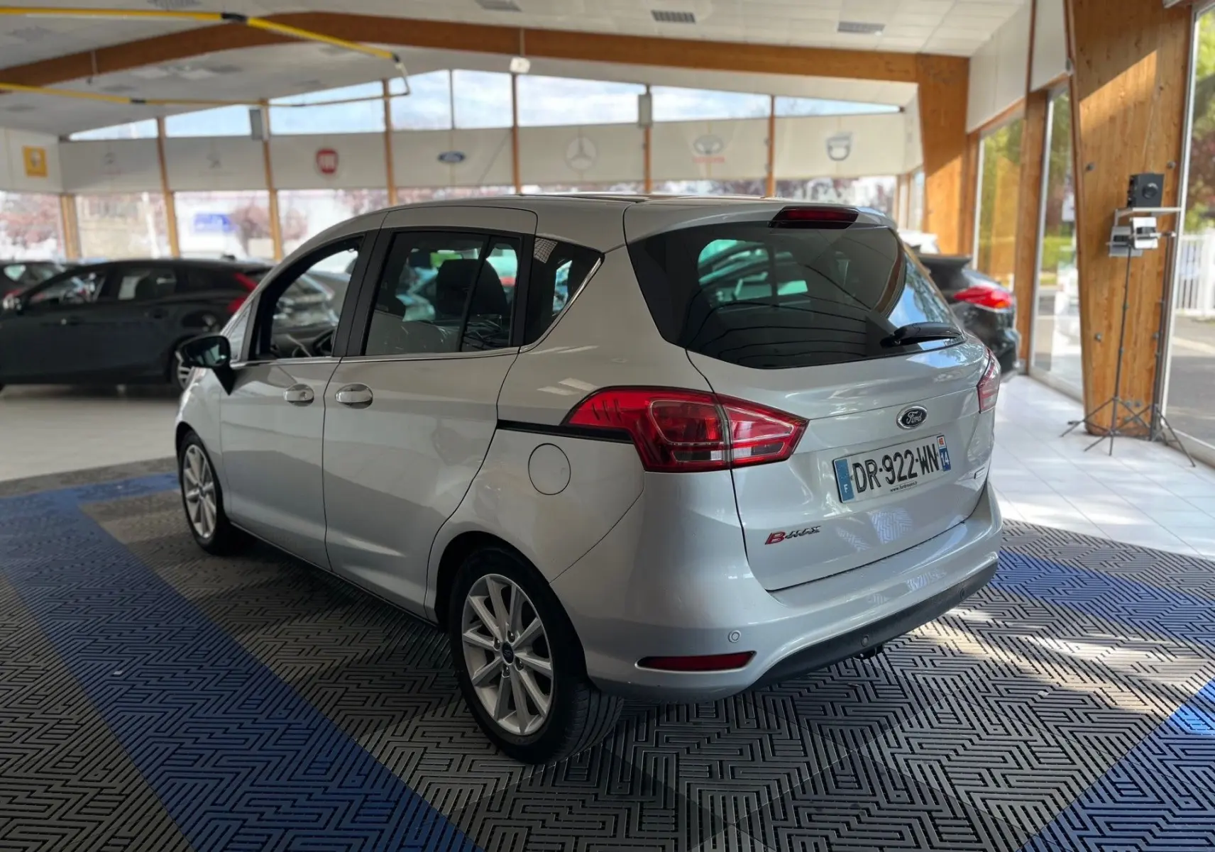 Ford B-MAX gris clair vue 3/4 arrière droit dans un showroom lumineux avec jantes alliage visibles.