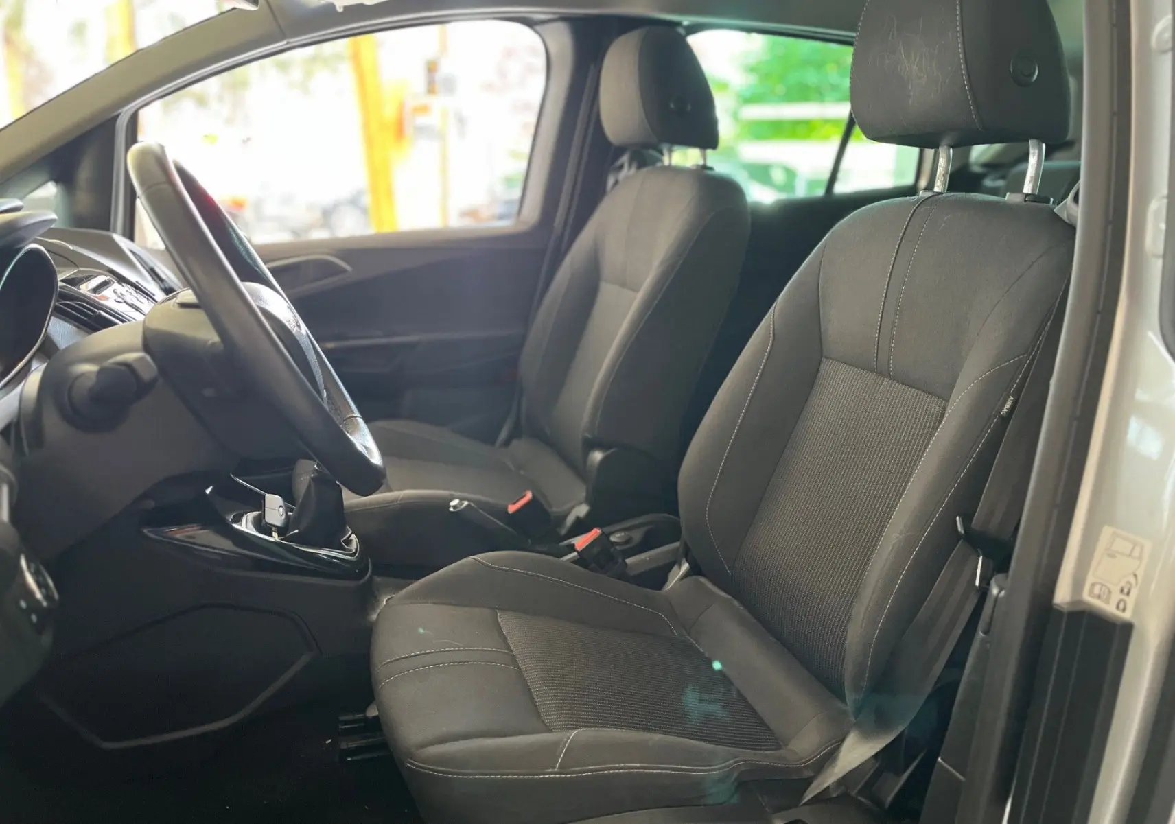 Intérieur avant du Ford B-MAX gris clair 2015, sièges tissu noir et volant cuir avec boîte manuelle visible.